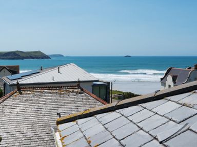 A coastal view with rooftops in the foreground and the ocean with waves and hills in the background at Egloskerry in New Polzeath