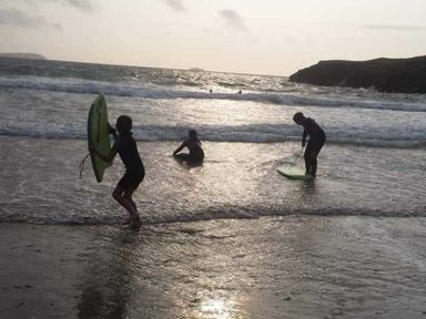 Children playing with bodyboards in the shallow water at the beach with waves and hills in the background