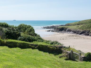 A coastal view with a sandy beach rocky shore green grass and a wooden gate at Egloskerry in New Polzeath