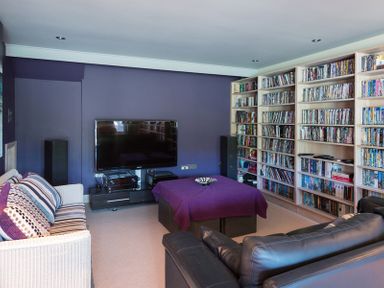 A living room with a television a large bookshelf and sofas at Egloskerry in New Polzeath