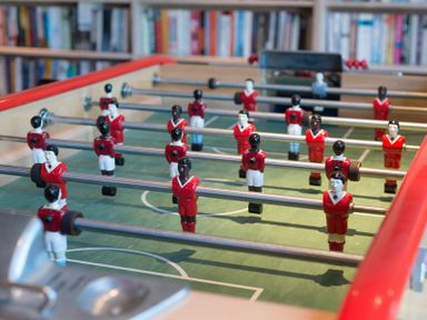 A foosball table with red and white player figures in front of a bookshelf at Egloskerry in New Polzeath