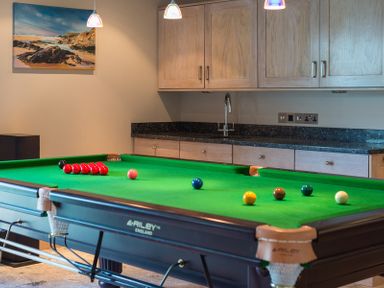 A room with a snooker table and wooden cabinets with a sink at Egloskerry in New Polzeath