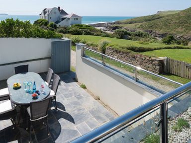 An outdoor patio with a table and chairs and a coastal view of the ocean and hills at Egloskerry in New Polzeath