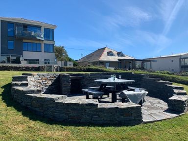 An outdoor stone seating area with a picnic table and benches in front of houses at Egloskerry in New Polzeath