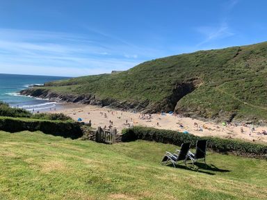 A sandy beach with people near the ocean surrounded by green hills and two chairs on grass at Egloskerry in New Polzeath
