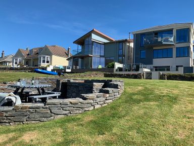 A grassy yard with stone seating area and picnic table in front of modern and traditional houses at Egloskerry in New Polzeath