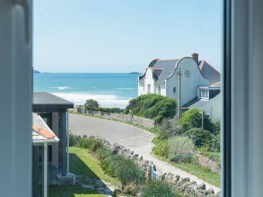 A view of a coastal road with houses bushes and the sea visible through a window at Egloskerry in New Polzeath