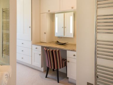 A built in vanity with a mirror above a marble countertop and a striped chair at Egloskerry in New Polzeath
