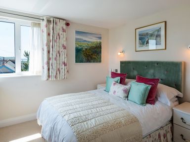 A bedroom with a bed with green and pink pillows a green headboard and two paintings on the wall at Egloskerry in New Polzeath
