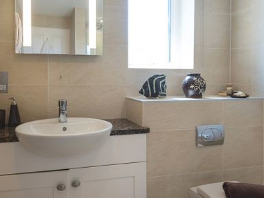 A bathroom sink with soap dispenser and decorative items on shelf near window at Egloskerry in New Polzeath