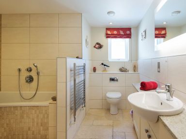 A bathroom with a bathtub shower toilet sink and a red towel on the counter at Egloskerry in New Polzeath
