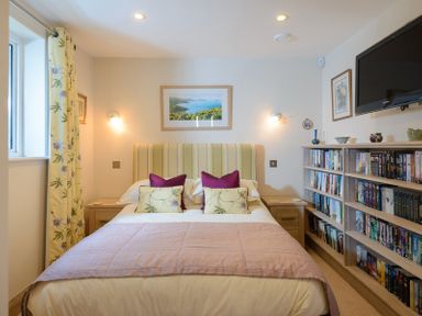 A bedroom with a bed and pillows next to a bookshelf and a window at Egloskerry in New Polzeath