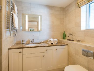 A bathroom with a sink cabinet countertop mirror towels and a window at Egloskerry in New Polzeath