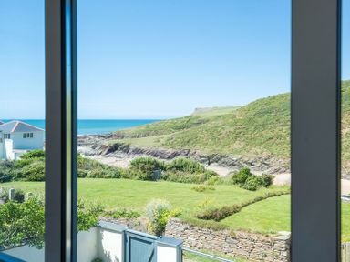 View of a grassy garden with stone wall and gate looking out to hills and the sea through a window at Egloskerry in New Polzeath