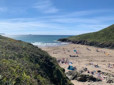 A sandy beach with people sunbathing and swimming surrounded by green hills at Egloskerry in New Polzeath