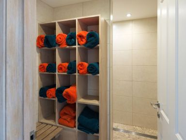 A storage shelf with rolled orange and dark green towels next to a tiled shower area at Egloskerry in New Polzeath