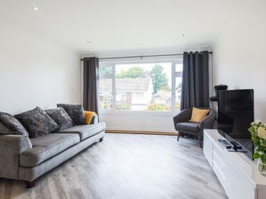 A living room with a grey sofa and armchair a television on a white console and a large window with curtains at Greenaway 4 Rockhaven Gardens in Rock