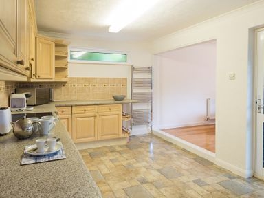 A kitchen with wooden cabinets a tiled floor and an open doorway leading to a room with wooden flooring at Greenaway 4 Rockhaven Gardens in Rock