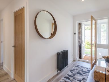 A hallway with a wooden door a round wall mirror a black radiator a patterned rug and an open glass door at Greenaway 4 Rockhaven Gardens in Rock