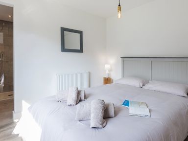 A bedroom with a bed with pillows towels and books a bedside table with a lamp a mirror and an open door to a shower at Greenaway 4 Rockhaven Gardens in Rock