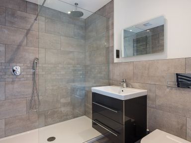 A bathroom with a walk-in shower a black vanity with a sink a mirror and a toilet at Greenaway 4 Rockhaven Gardens in Rock