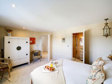 A bedroom with a bed with pillows and a tray of food a white cabinet two wicker chairs and an open door leading to a bathroom at Seahaven in Port Isaac