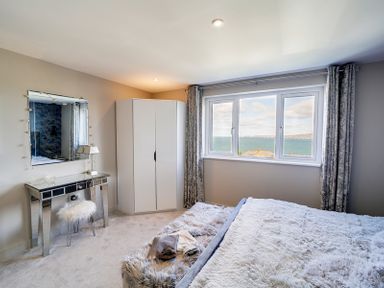 A bedroom with a mirrored dressing table and chair wardrobe bed and window overlooking the sea at Seahaven in Port Isaac