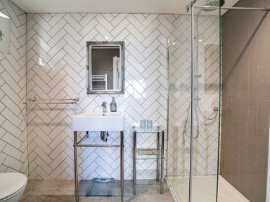 A bathroom with a shower, sink, mirror, and glass shelves at Seahaven in Port Isaac