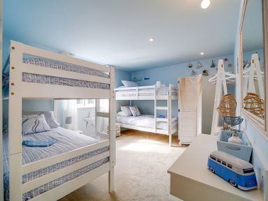 A bedroom with two white bunk beds a dresser with decorative items and wall-mounted sailboat decorations at Seahaven in Port Isaac