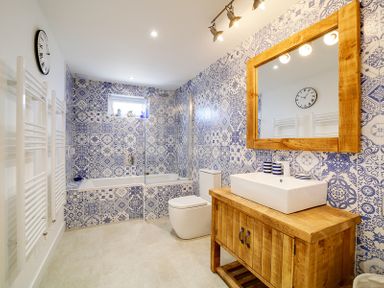 A bathroom with a wooden vanity and mirror blue patterned tiles bathtub toilet and wall clock at Seahaven in Port Isaac
