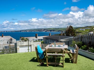 A garden with a wooden picnic table and benches on artificial grass overlooking the sea at Seahaven in Port Isaac