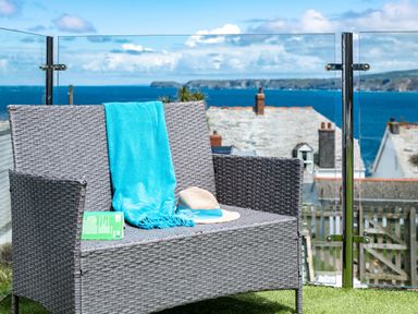 A wicker bench with a turquoise towel a hat and a book on a balcony overlooking the sea and rooftops at Seahaven in Port Isaac