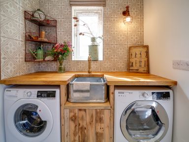 A laundry room with washing machine, dryer, sink, wooden countertop, shelving, and window at Seahaven in Port Isaac
