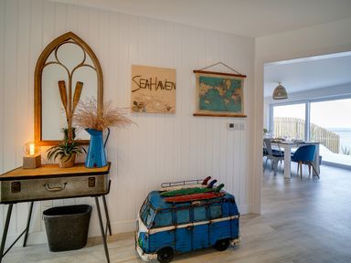 An entryway with a table holding plants and a lamp next to a blue decorative van with surfboards a world map and artwork on the wall at Seahaven in Port Isaac