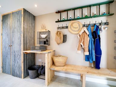 A mudroom with coats hanging on hooks a wooden bench a wooden cabinet with corrugated metal doors and baskets on the floor at Seahaven Port Isaac
