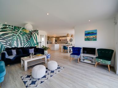 An open plan living space with a sofa, coffee table, two knitted pouffes, chairs, a television, dining table, and kitchen at Seahaven in Port Isaac