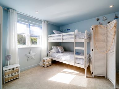 A bedroom with white bunk beds two small bedside tables and a window with white curtains at Seahaven in Port Isaac