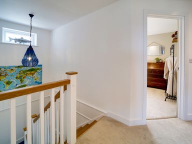 A stairway with wooden handrails and blue chandelier next to a room with a wooden dresser and a robe on a rack at Seahaven in Port Isaac