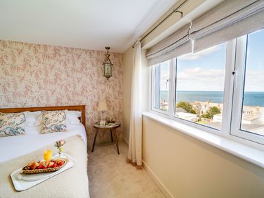 A bedroom with a bed with floral pillows a nightstand and a window showing a sea view at Seahaven in Port Isaac