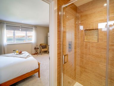 A bedroom with a bed and window next to a bathroom with a glass shower at Seahaven in Port Isaac