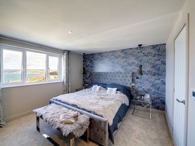 A bedroom with a large bed and a blue patterned wallpaper overlooking the sea at Seahaven in Port Isaac
