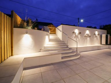 An outdoor area with tiled flooring stairs with metal railing wooden fence and wall lights at Seahaven Port Isaac
