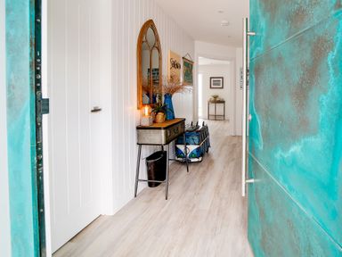 A hallway with a decorative mirror a lamp and vase on a console table and a blue front door at Seahaven in Port Isaac