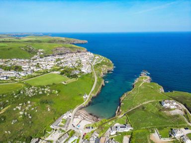 An aerial view of a coastal village with green fields and a road leading to the sea at Seahaven in Port Isaac