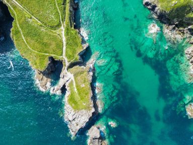 An aerial view of a rocky coastline with green grassy cliffs and turquoise water at Seahaven in Port Isaac