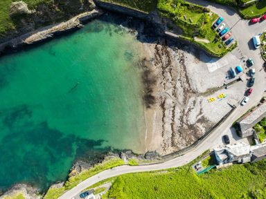An aerial view of a small coastal bay with clear green water a rocky beach cars parked near the shore and kayaks on the beach at Seahaven in Port Isaac
