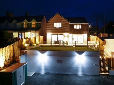 A modern house with a lit backyard patio and glass fence at Seahaven in Port Isaac