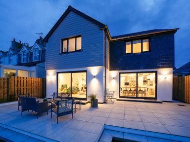 A modern two-story house with patio furniture on a tiled patio and large sliding glass doors at Seahaven in Port Isaac