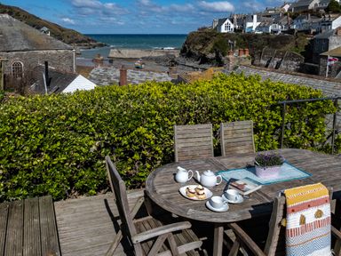 An outdoor wooden table with tea set and scones on a deck overlooking houses and the sea at Grey Roofs in Port Isaac