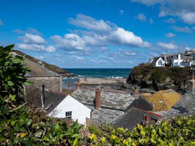 Rooftops of houses near a rocky coastline with the sea and partly cloudy sky at Grey Roofs in Port Isaac
